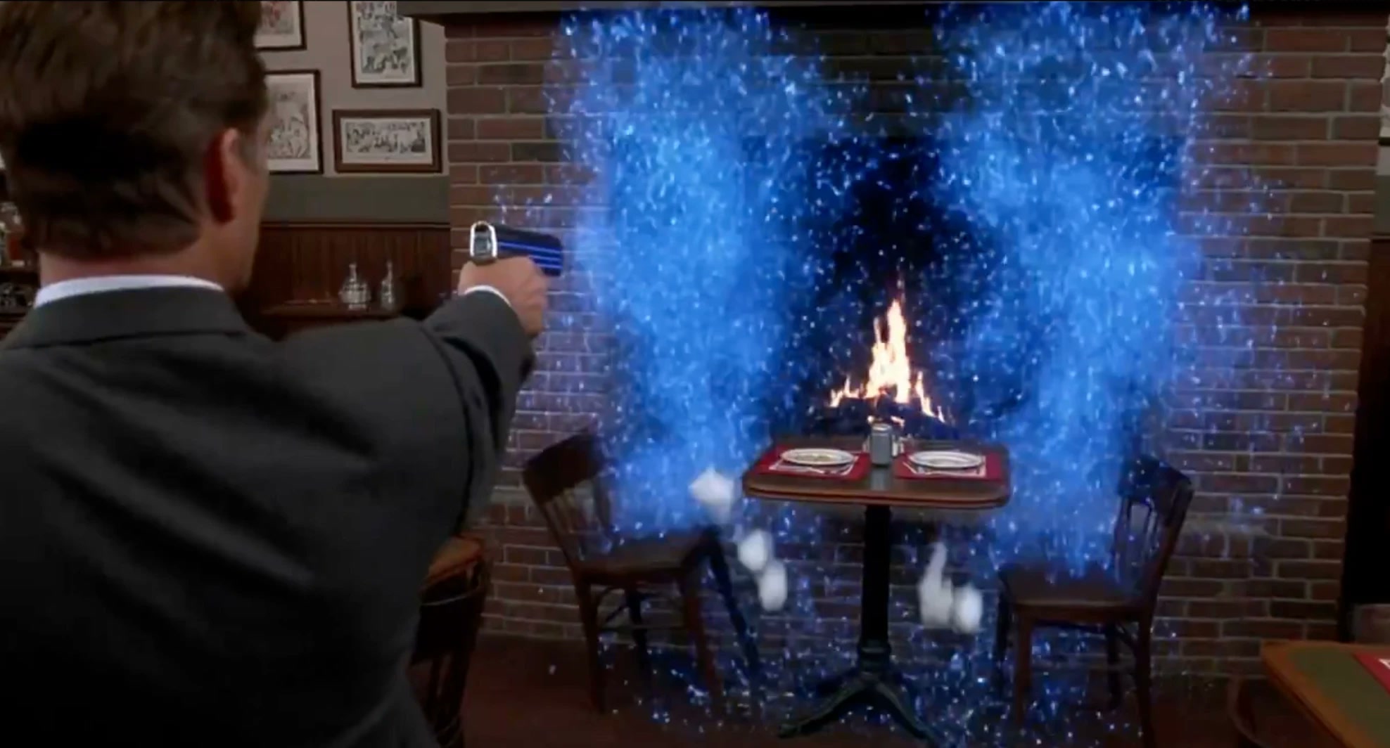 A man in a suit, seen from behind, fires a glowing blue pistol at a restaurant brick wall that bursts into blue particles around a lit fireplace and a set table
